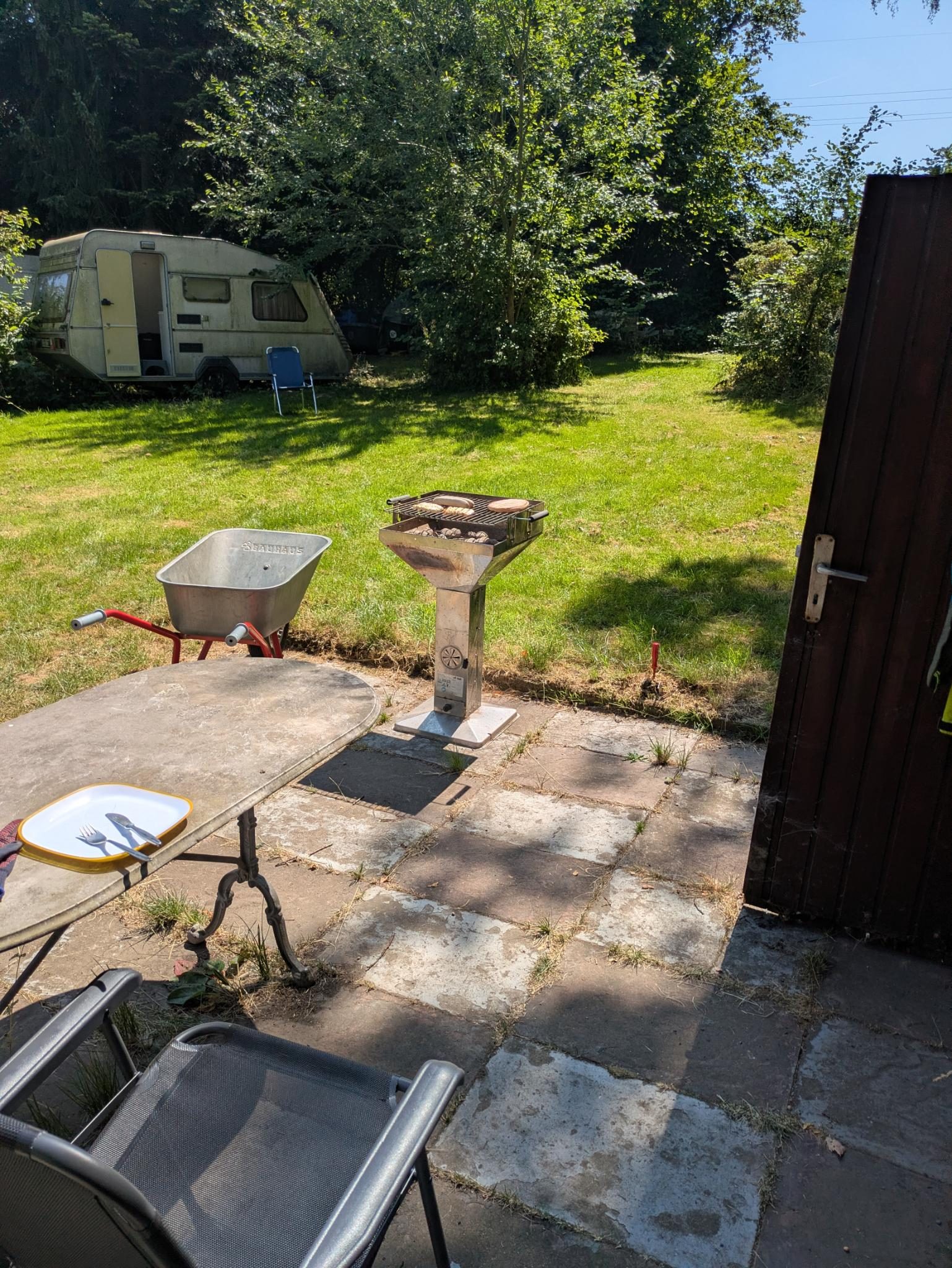 Sonniger Garten mit Grill, Terrasse und Schatten unter Bäumen